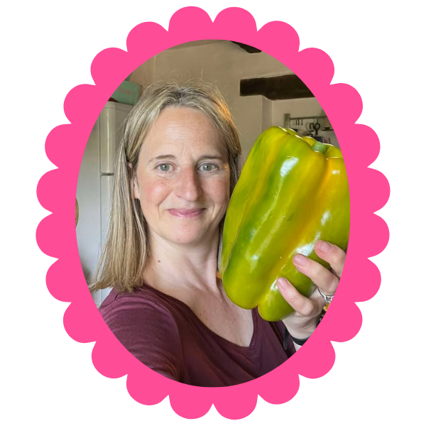 Kristin, a woman with fair hair, holds a giant green pepper next to her head.